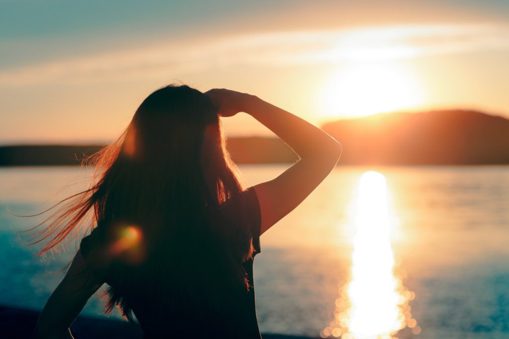 Silhouette of woman gazing at the light of the rising sun on the horizon.
