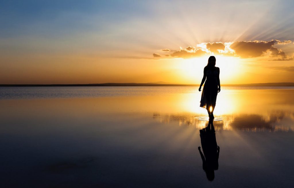Woman illuminated by the sun walking along a lake